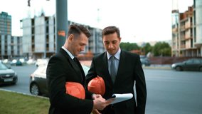 4k. Two Young attractive architects standing and looking at the textpad plan of construction. They decide to put on orange helmets and walk and review result of new building making. Middle shot. Crane - Powered by Shutterstock - Get 15% off with code: PIKWIZARD15