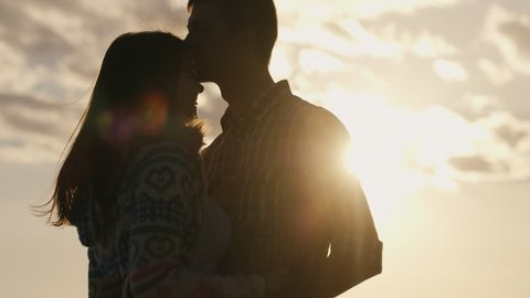 Silhouette of a young couple in love on the background of sky and sun, looking at each other