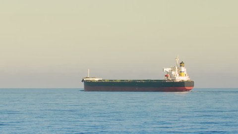 Large panamax bulk carrier ship sailing in open ocean, side view tracking shot. Bulk Carrier is a merchant vessel, designed to transport unpackaged bulk cargo, such as grain, ore, coal.