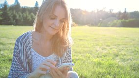 High quality 10bit footage of Happy Smiling Girl Using a SmartPhone in City Park Sitting on Grass. Made from 14bit RAW.