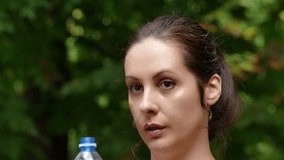 A young woman runs and drinks water in a beautiful green park in slow motion, Running and Drinking Water During Training, 4 K Video Clip