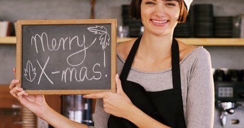 Portrait of Caucasian waitress showing slate with merry x-mas sign in coffee 4k