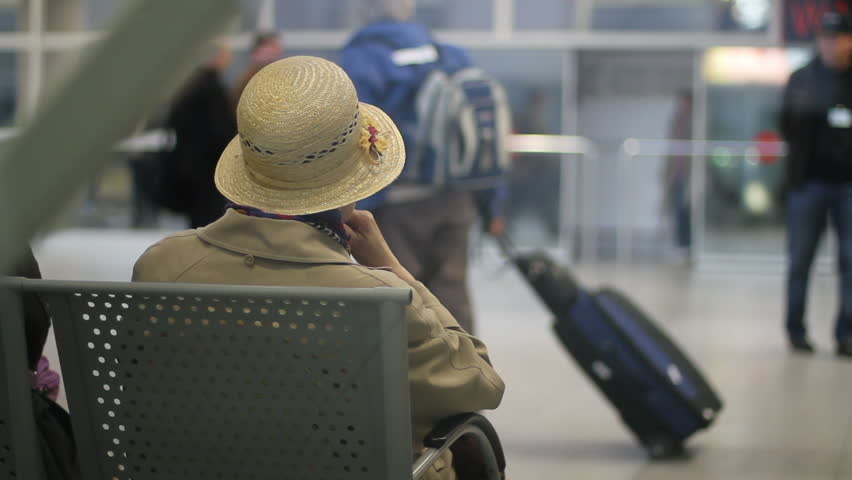 Elderly woman in straw hat waits at the airport