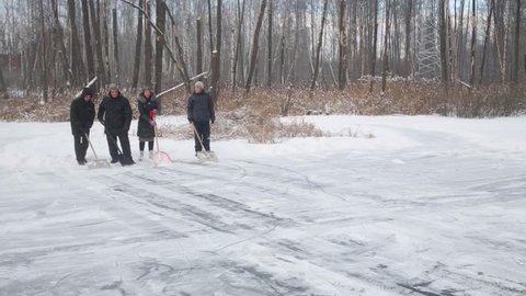 The four people with shovels clean snow from ice skating rink