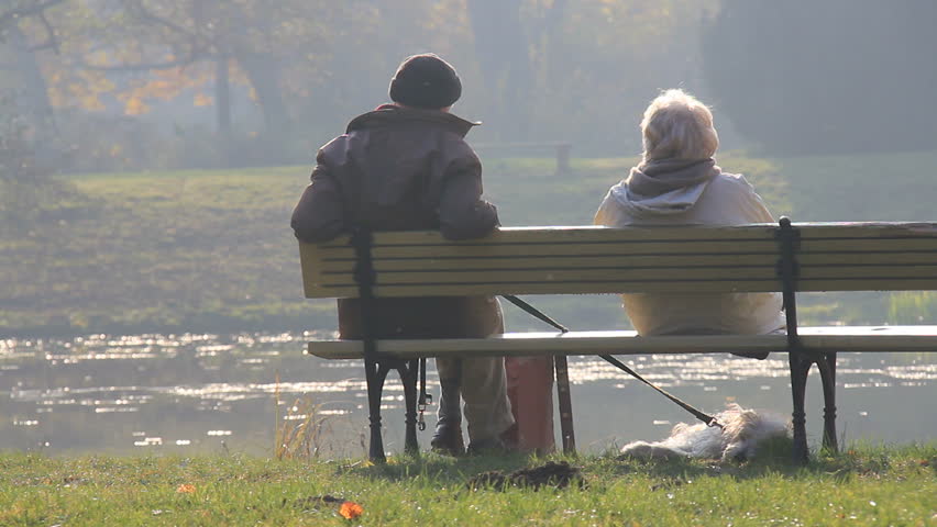Elderly couple and a dog sitting quietly on park bench