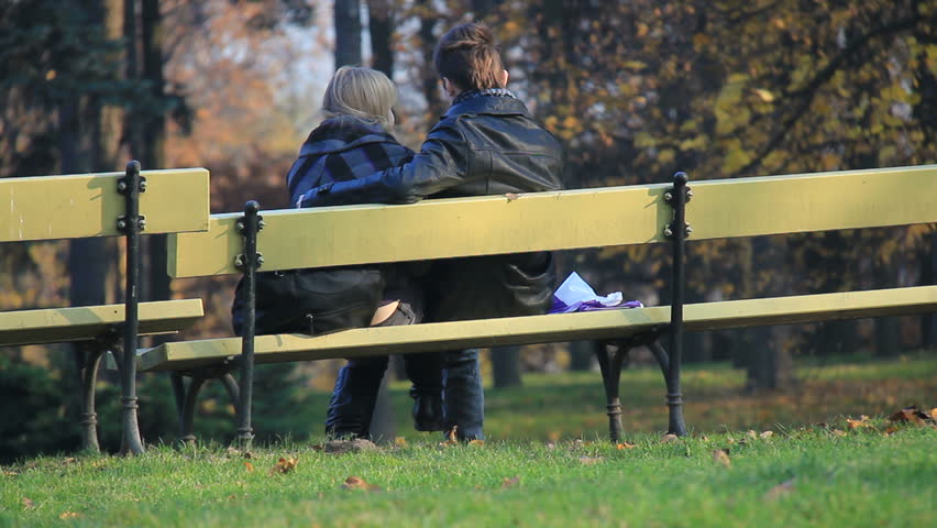 Young couple snuggle on a bench in park