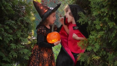 Children wearing witch costumes with hats playing with pumpkin with a burning candle in autumn Park on Halloween. boy and girl scare each other. Kids trick or treat.