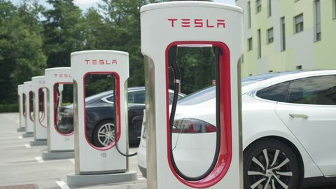 LJUBLJANA, SLOVENIA - JULY 10 2016: White and black Tesla autonomous electric cars refilling energy at free of charge super fast charging station on parking lot. Luxury vehicles charging battery