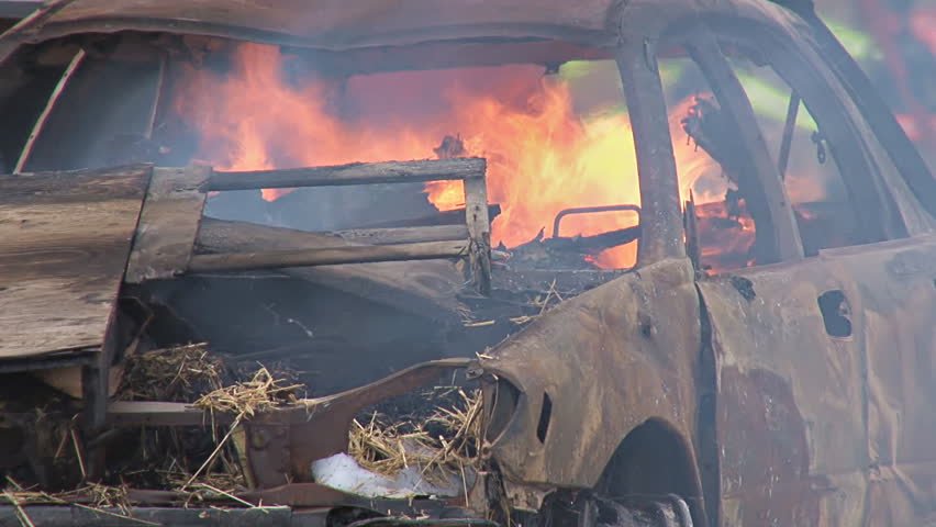 Burning car, general shapes of firefighting crew seen through flames.