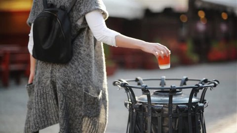 Female throwing empty coffee cup on the trash at the street in the city, On a background cozy cafe