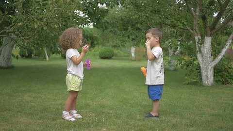 The little girl and boy are blowing bubbles in the garden