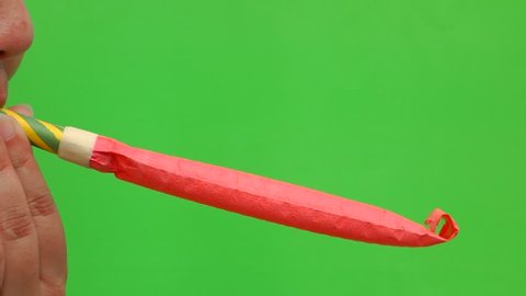 female blowing a colorful party horn in front of the green screen