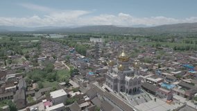 Pigeons fly over a golden domed mosque among stunning mountain scenery in central China. Aerial panning video. 