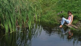 Girl sitting on the shore of the pond. Long shot, Establishing shot in Russia, Tvertca river. Contains child/girl 8-9 years.