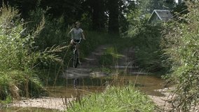 A girl with a bicycle passes a puddle on a country road. ?oncept of overcoming and challenge difficulties. Medium Shot, Establishing Shot, contains teen 10-12 years.