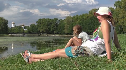 Mother and daugther sitting on the meadow in the park. Medium Shot, Establishing Shot, contains people: teen 10-12 years, fimale 30-40 years. Russia, Tvertca river. 