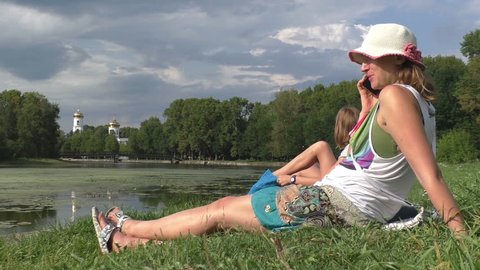 Young woman speaks by telephone on meadow next to the river. Medium Shot, Establishing Shot, contains caucasian ethnicity, teen 10-12 years, fimale 30-40 years. Russia, Tvertca river.