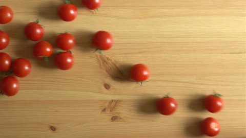 Many tomatoes roll on a wooden surface. Slow Motion. Top view.