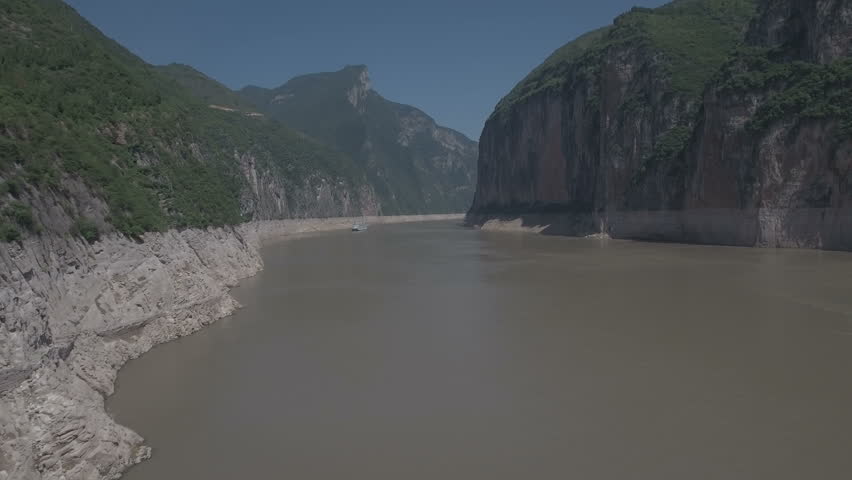 Aerial drone flight through the sceni Qutang Gorge on the Yangtze river in central China. A seemingly tiny cruise ship sails through the massive cliffs in the distance.. D-log profile on DJI Phantom.