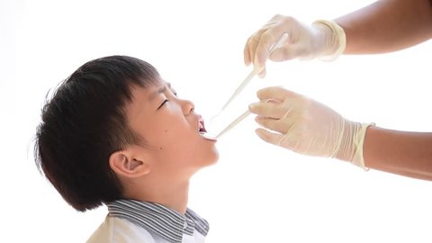 Dentist checking young unhappy asian boy teeth by equipment on white background.