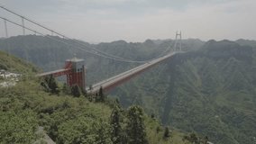 Stunning panoramic aerial view of the Aizhai suspension bridge in China. Halfway through the video the camera tilts downwards to reveal the bridge and underlying mountain valley and hairpin road.