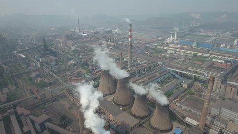 Aerial shot of polluting coal fired power reactors on the grounds of a huge steel producing factory in China. Camera tilting down halfway during the drone flight.
