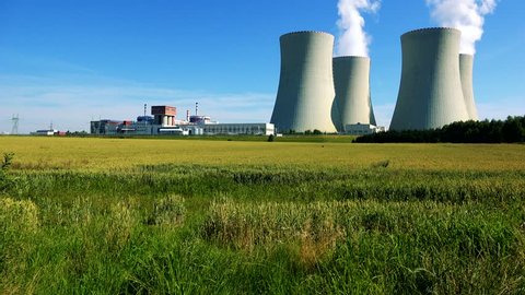 factory (nuclear power station) - closeup of buildings and smoke from chimney - field with plants and blue sky