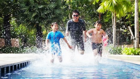 Two Asian boys racing with their father in a pool.