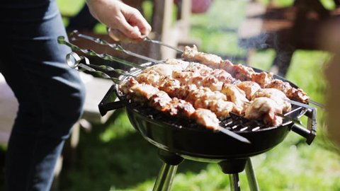 leisure, food and drinks, people and holidays concept - man cooking meat on barbecue grill for his friends at summer outdoor party