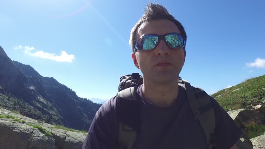 man with sunglasses hiking, walking, trekking outdoors on mountain trail path toward river in sunny day, 4k selfie pov (point of view)