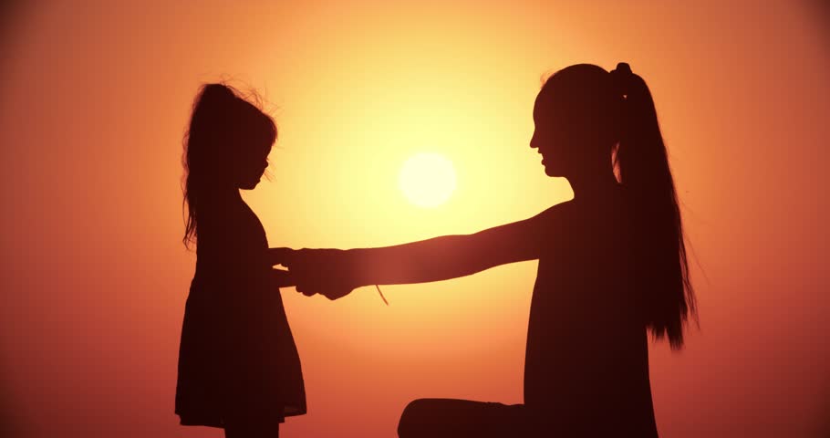 silhouette of mother and little daughter playing at sunset, slow motion, close-up