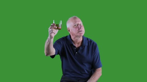 Older man in blue shirt raising a glass in toast on green.