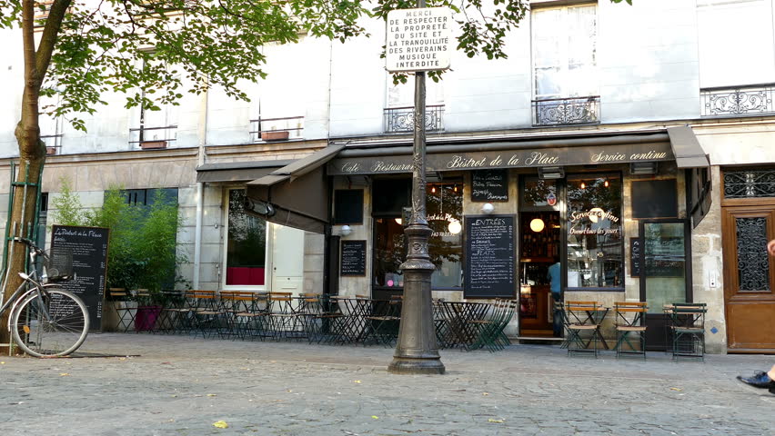 Paris, France. A beautiful young woman leaning on a lamppost, next to a bistro in an old cobbled square early on a Sunday morning.