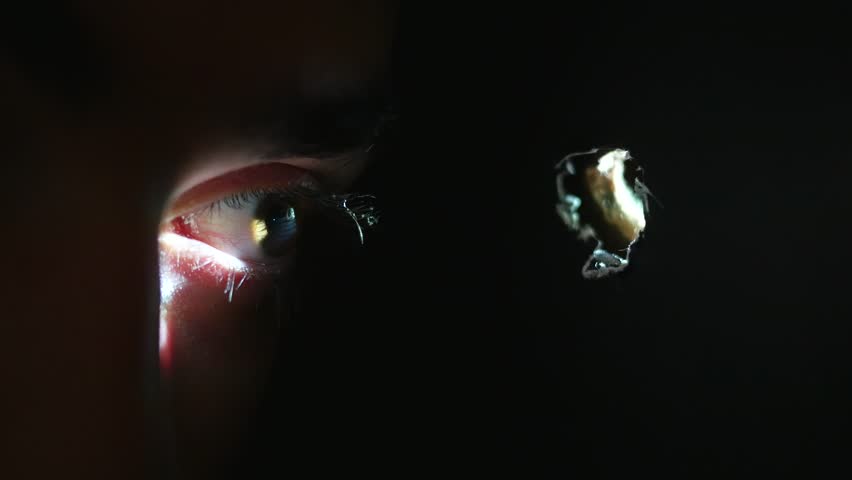 Eye looking trough a small hole. Light is coming from this hole.