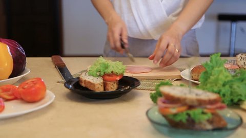 Close up of a young woman preparing a baguette lunch sandwich with fresh vegetables and deli cold cut meats