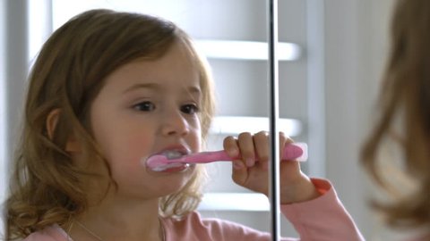 Little girl diligently brushing his teeth in the mirror.