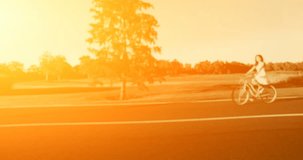 4K shooting: Young woman riding vintage bicycle in sunset country road. Active people. Side view. Video processed in orange glow