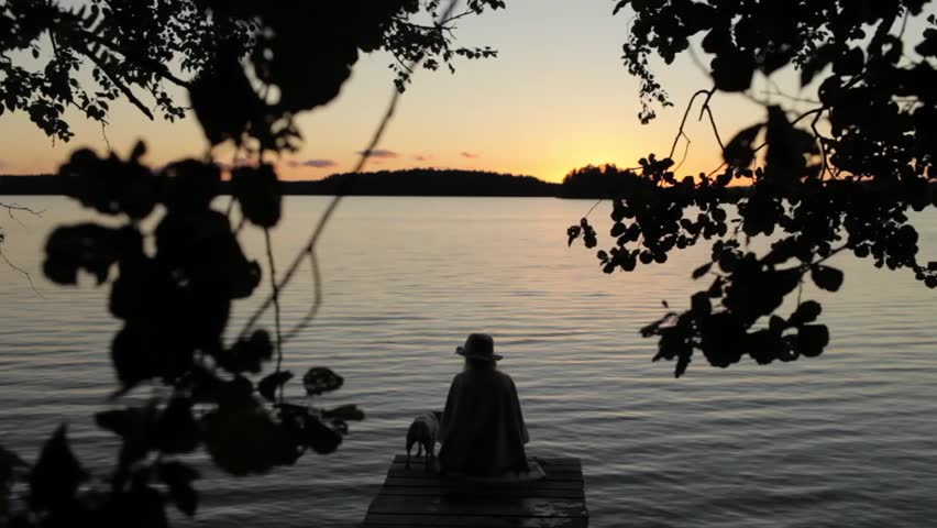 Woman With a Dog Sitting on the Dock of the Lake at Sunset