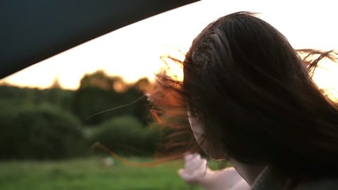 Happy woman smiles, enjoys traveling by car. She reaches her arm through the window of a car. Wind blows hair. Slow mo