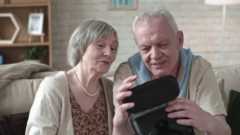 Elderly man and senior woman sitting on sofa and inspecting virtual reality headset