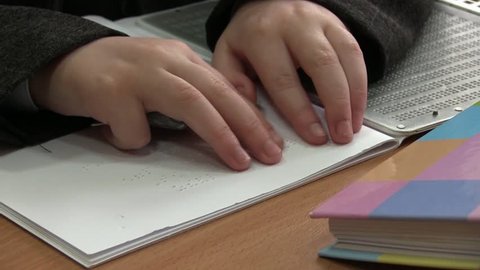 Kid Reading Braille. The child learns to read Braille on a sheet of paper sitting at the desk in the school