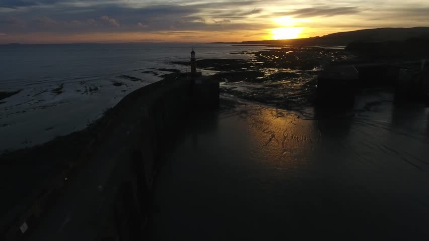 Aerial view flying towards and past a lighthouse onto the beach at sunrise.
