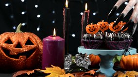 Halloween party table with spooky hand with long black nails sneaking over chocolate cupcakes.  - Powered by Shutterstock - Get 15% off with code: PIKWIZARD15
