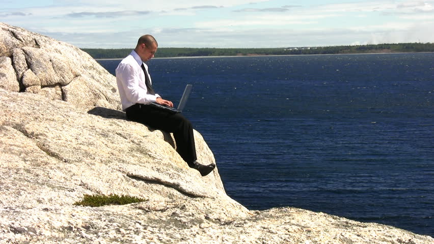 Businessman using Laptop on cliffs by the ocean. Shot in 1080i