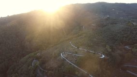  aerial shot gorgeous drone flight over an italian nature, a serpentine  road situated on the hills, with some medieval architecture,  europe, strong sunset light with the sun flare
