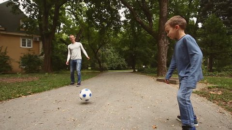 Father and his son playing soccer on a park road. 