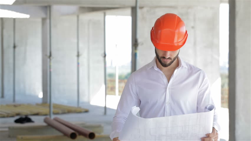 Male architector looking at the plan of building under construction. Young caucasian construction engineer looking at the ceiling at the building under construction. Bearded construction manager
