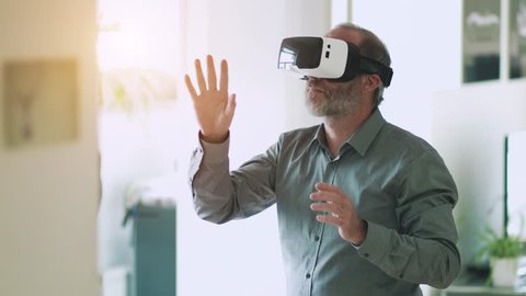Technology VR - Mature businessman wearing virtual reality technology googles  VR Glasses to work with in modern bright office. This new technology offers new 3D dimensions