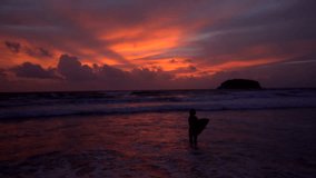 Silhouette of beautiful woman standing in the sea  with surfboard during amazing sunset - video in slow motion
