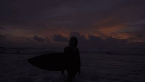 Silhouette of beautiful woman walking in the sea  with surfboard during amazing sunset - video in slow motion